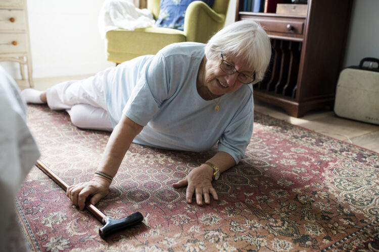 Elderly woman on the floor reaching for her cane after a fall, emphasizing the importance of medical alert systems for quick assistance.