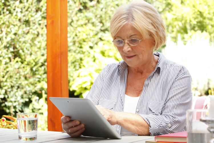 A member in communication sitting outdoors using a tablet, with a glass of water and book on the table