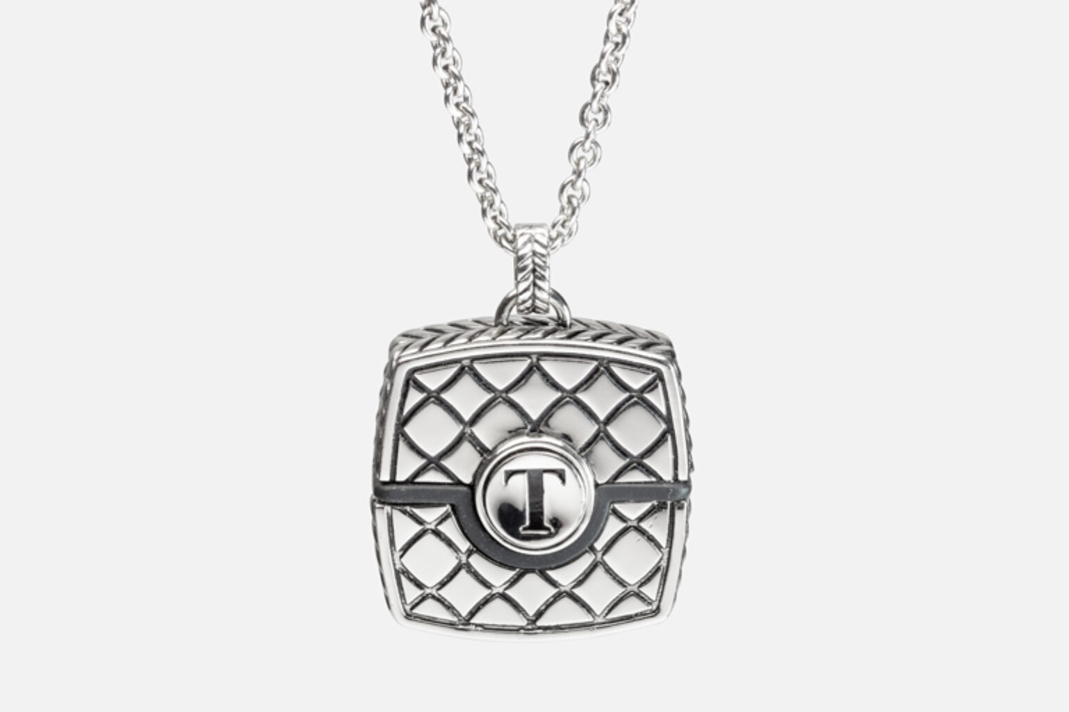 Close-up of silver necklace pendant with a quilted pattern and a "T" emblem