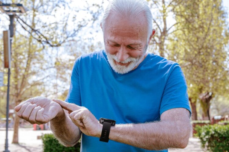 An older man outdoors wearing a blue shirt and checking his LifeStation Sidekick smartwatch